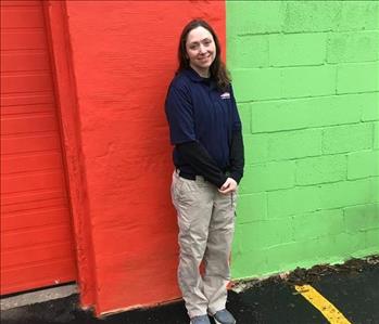 A female SERVPRO employee standing in front of a orange and green building. 