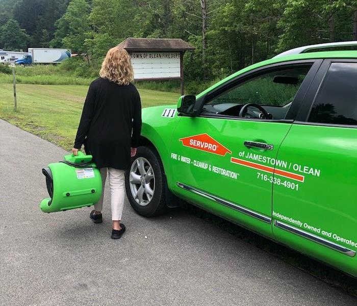 female carrying a green air mover down a street next to a green SERVPRO car